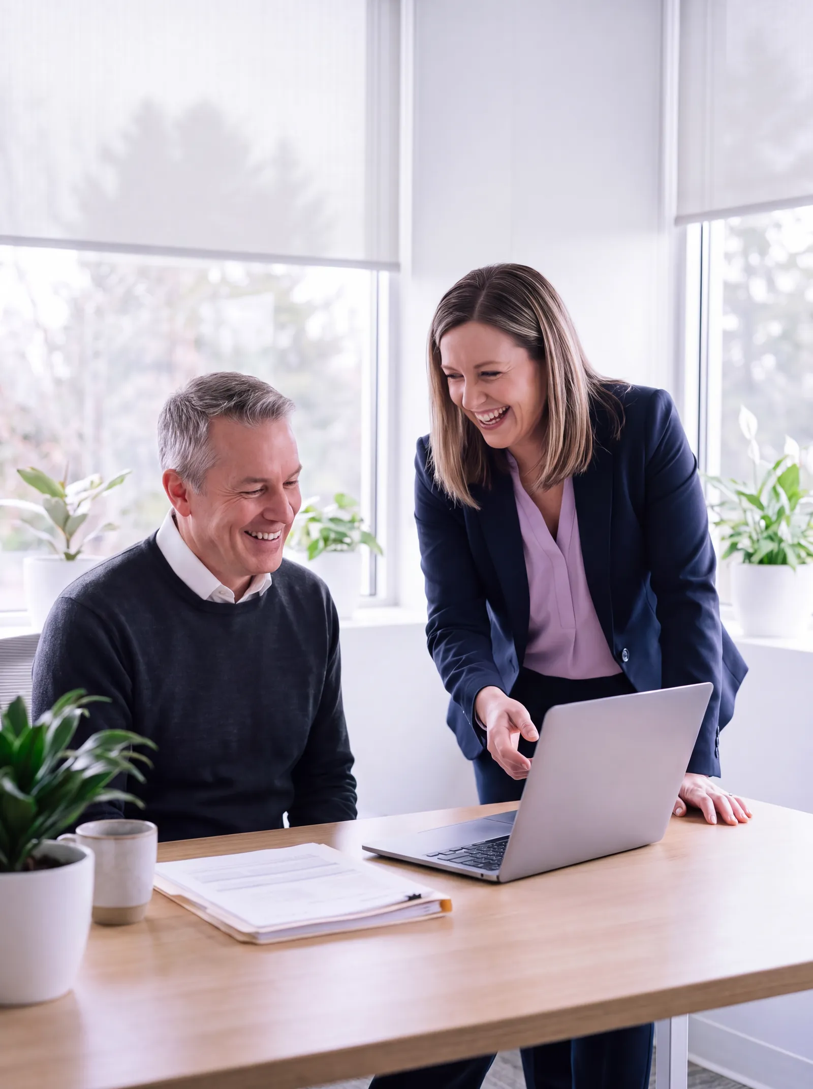 An accountant shows her client something on the laptop in a bright office, and they share a laugh